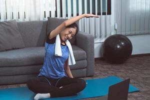 Asian woman stretching during a yoga class with a trainer at her laptop computer at home. photo