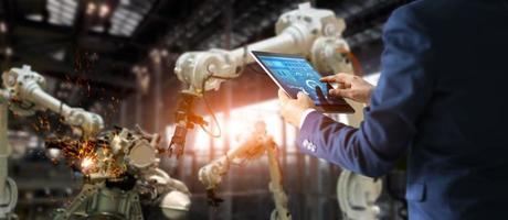 Industrial engineer manager using tablet check and control automation robot arms machine in intelligent factory. Welding roboticts and digital manufacturing operation. Industry 4.0 concept photo