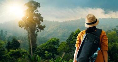 Female traveller with backpack relax and enjoy the natural scenery on mountain landscape. Trekking in tropical rain forest.