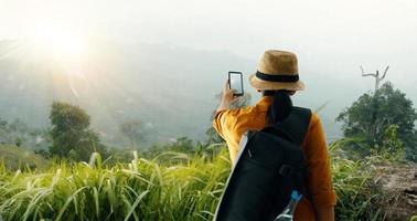 Backpacker using smartphone taking picture beautiful landscape on mountain peak while exploring, trekking in tropical rain forest of Asia photo