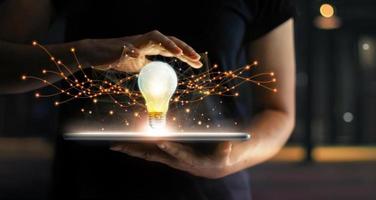 Abstract. Innovation. Hands holding tablet with light bulb future technologies and network connection on virtual interface background, innovative technology in science and communication concept photo