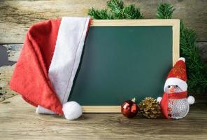 Blackboard With Red Santa Hat And Christmas snowman toy on old wooden background. photo