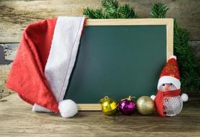 Blackboard With Red Santa Hat And Christmas snowman toy on old wooden background. photo