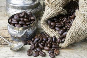 Silver cup and Coffee beans in sackcloth bag on wooden background photo