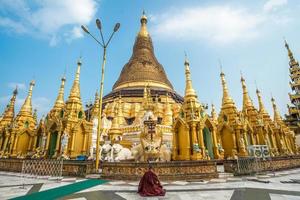 monje budista sentado y meditando frente a la pagoda de shwedagon, un hito icónico en el centro de yangon, myanmar. foto