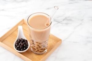 Tapioca pearl ball bubble milk tea, popular Taiwan drink, in drinking glass with straw on marble white table and wooden tray, close up, copy space. photo