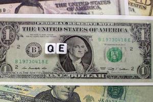 QE written on cube with dollars background for quantitative easing concept. photo