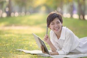 happiness emotion relaxing time of asian younger woman with book and pen in summer park