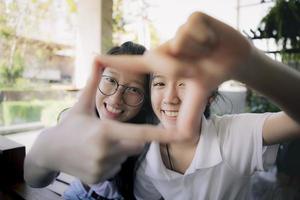 Dos signos de mano de adolescentes asiáticos como marco de fotos con cara de felicidad detrás