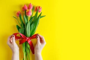 Woman ties bow on bouquet of tulips. Colorful fresh spring flowers on yellow background. photo