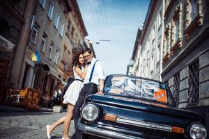 pareja joven, mujer y hombre guapo posando cerca de un auto retro negro foto