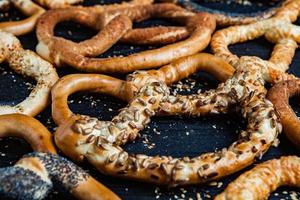 Fresh prepared homemade soft pretzels. Different types of baked bagels with seeds on a black background. photo