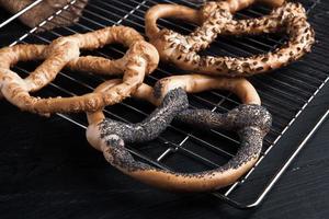 pretzels suaves caseros recién preparados. diferentes tipos de panecillos horneados con semillas sobre un fondo negro. foto