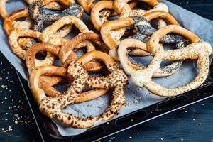 Fresh prepared homemade soft pretzels. Different types of baked bagels with seeds on a black background. photo