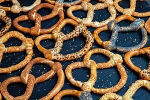 Fresh prepared homemade soft pretzels. Different types of baked bagels with seeds on a black background. photo
