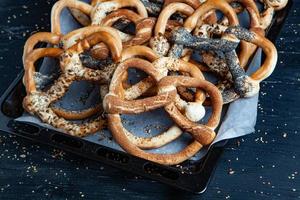 Fresh prepared homemade soft pretzels. Different types of baked bagels with seeds on a black background. photo