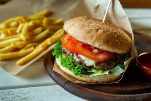 big tasty burger on a wooden table and french fries. Delicious burger with beef, tomato, cheese and lettuce. photo