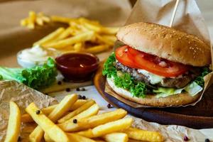 gran hamburguesa sabrosa en una mesa de madera y papas fritas. deliciosa hamburguesa con carne de res, tomate, queso y lechuga. foto