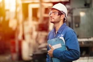 retrato del libro manual de servicio de máquina de educación de ingeniero inteligente trabajador feliz de pie con orgullo en el fondo de la industria pesada. foto