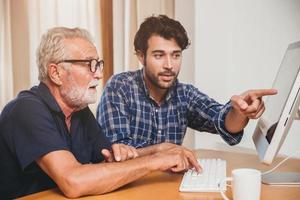 joven o hijo enseñando a su abuelo padre anciano aprendiendo a usar la computadora en casa. foto