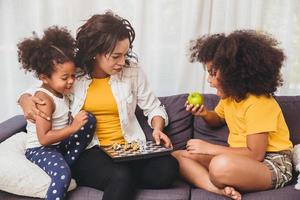 Single mom good care, teaching her childs to be genius and clever little girls learning to play chess boardgame eating fruit for healthy. photo