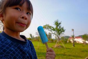 Close-up portrait of the beautiful, cute, little lady, eating ice cream in watermelon in her mouth, with heart gate and blue sky background. photo