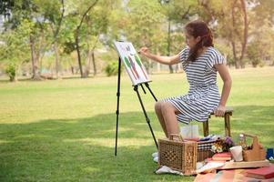 A half-Thai-European girl  is sitting on the wooden bench and painted on the canvas placed on a drawing stand photo