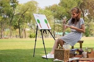 A half-Thai-European girl  is sitting on the wooden bench and painted on the canvas placed on a drawing stand photo