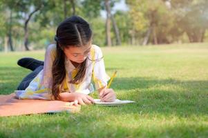 una chica medio tailandesa descansa y escribe en un cuaderno mientras aprende fuera de la escuela en un parque
