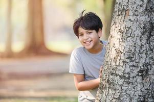 un niño mitad indio tailandés juega en secreto detrás de un gran árbol en un parque mientras aprende fuera de la escuela foto