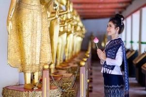 Attractive Thai woman in an ancient Thai dress holds a fresh flowers paying homage to Buddha to make a wish on the traditional Songkran festival in Thailand