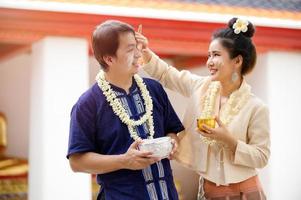 hombres y mujeres tailandeses vestidos con trajes tailandeses usan polvo soluble en agua para pintarse las mejillas con alegría al celebrar el festival del agua de songkran foto