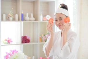 A beautiful Asian woman uses spa mud and tomato slice for facial treatment photo