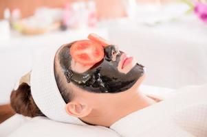 una hermosa mujer asiática usa lodo de spa y rodaja de tomate para el tratamiento facial foto