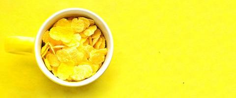 Yellow cup with cornflakes on bright yellow background. photo