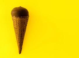 Vanilla ice cream with cranberry jam in a sugar cone dipped in chocolate on light yellow background. photo