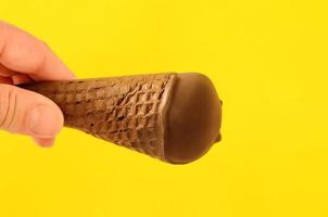 Man holding in hand vanilla ice cream with cranberry jam in a sugar cone dipped in chocolate. photo