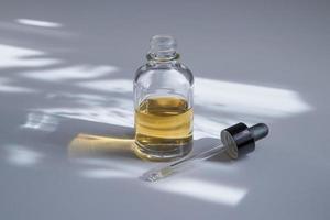 Open glass dropper bottle with skin care cosmetic. Butter, serum, or tincture with hard shadow
