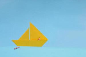 Yellow Paper boat and Miniature People On Blue Background photo