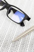 Pen and glasses rest on stock price detail financial newspaper photo