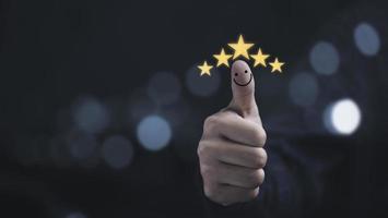 el pulgar se levanta con cinco estrellas amarillas y sonríe para la satisfacción del cliente y la evaluación después de usar el concepto de producto y servicio. foto