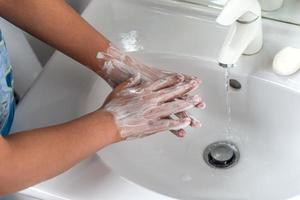 Woman washing hand with soap foam and tap water in bathroom. Hand clean under faucet on sink for personal hygiene to prevent flu and coronavirus. Good procedure of hand wash to kill bacteria, virus photo
