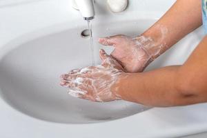 mujer lavándose las manos con espuma de jabón y agua del grifo en el baño. limpie a mano bajo el grifo del fregadero para la higiene personal para prevenir la gripe y el coronavirus. buen procedimiento de lavado de manos para matar bacterias, virus foto