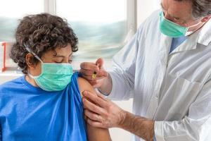 médico varón con mascarilla protectora guantes de látex que administran vacunación intramuscular brazo protegido del paciente foto