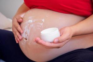 Pregnant Woman applying stretch marks cream on her belly photo