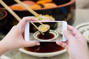 Taking photo of sushi roll in chopsticks