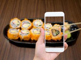 mano femenina tomando fotos de maki sushi con teléfono móvil