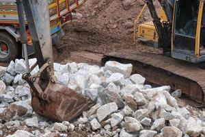excavadora amarilla o camión macro que trabaja en el sitio de construcción de la casa transporta rocas blancas foto