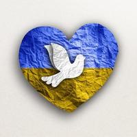 Flag of Ukraine in paper heart shape with dove of peace. photo