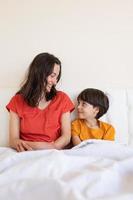 A child with mom sit on the bed, a woman and a boy in pajamas photo